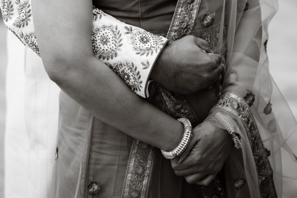 An Indian couple at their wedding hold each other. He is wearing a sherwani and she is wearing a lehenga