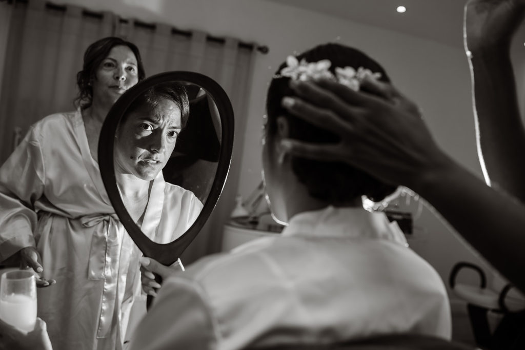 A bride examines her hair in a mirror while her mother looks on in a hair salon before her Caribbean Destination Wedding photographed by TKM Photography located in Roatan, Honduras and Durham Region, Ontario