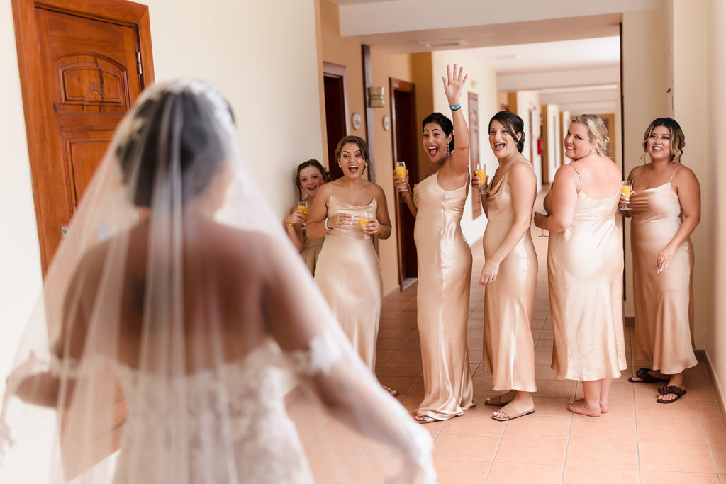 Bridal party reacts positively to seeing the bride for the first time fully dressed in her wedding dress before a Caribbean Destination Wedding photographed by TKM Photography located in Roatan, Honduras and Durham Region, Ontario