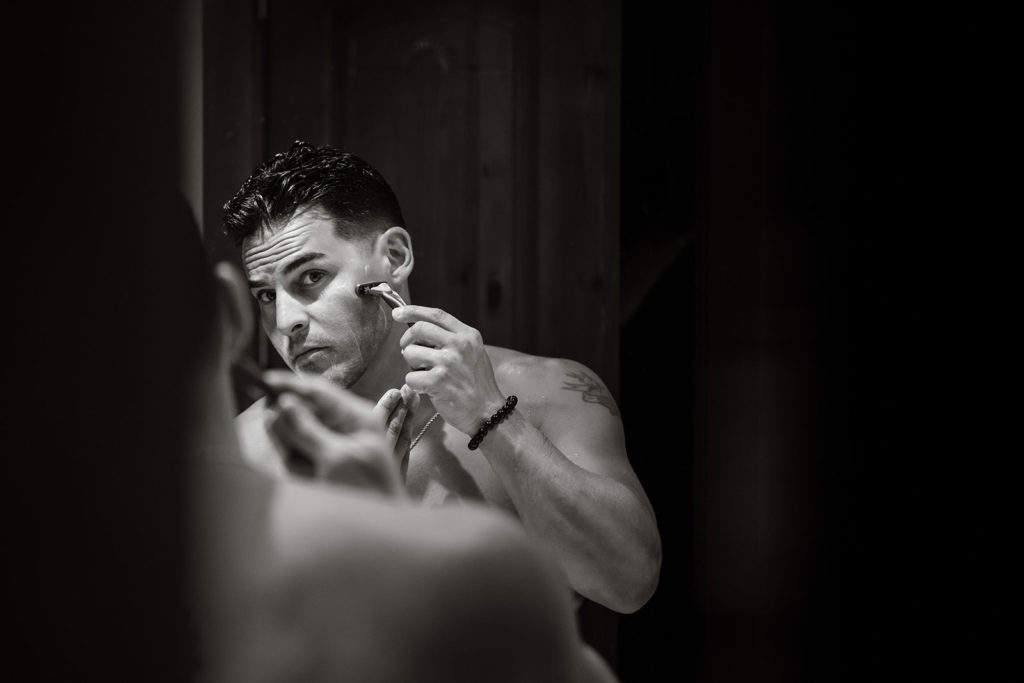 A groom shaves in a mirror before a Caribbean Destination Wedding photographed by TKM Photography located in Roatan, Honduras and Durham Region, Ontario