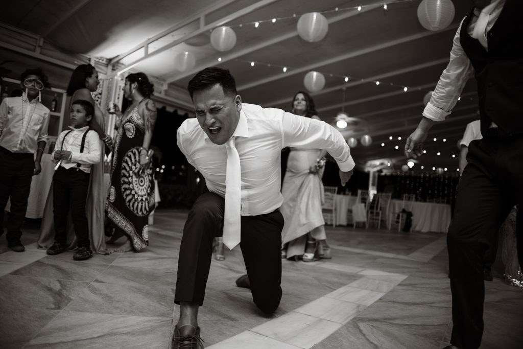 The best man kneels in a dance move at a Caribbean Destination Wedding photographed by TKM Photography located in Roatan, Honduras and Durham Region, Ontario, while her sister plays traditional wedding songs behind them. 